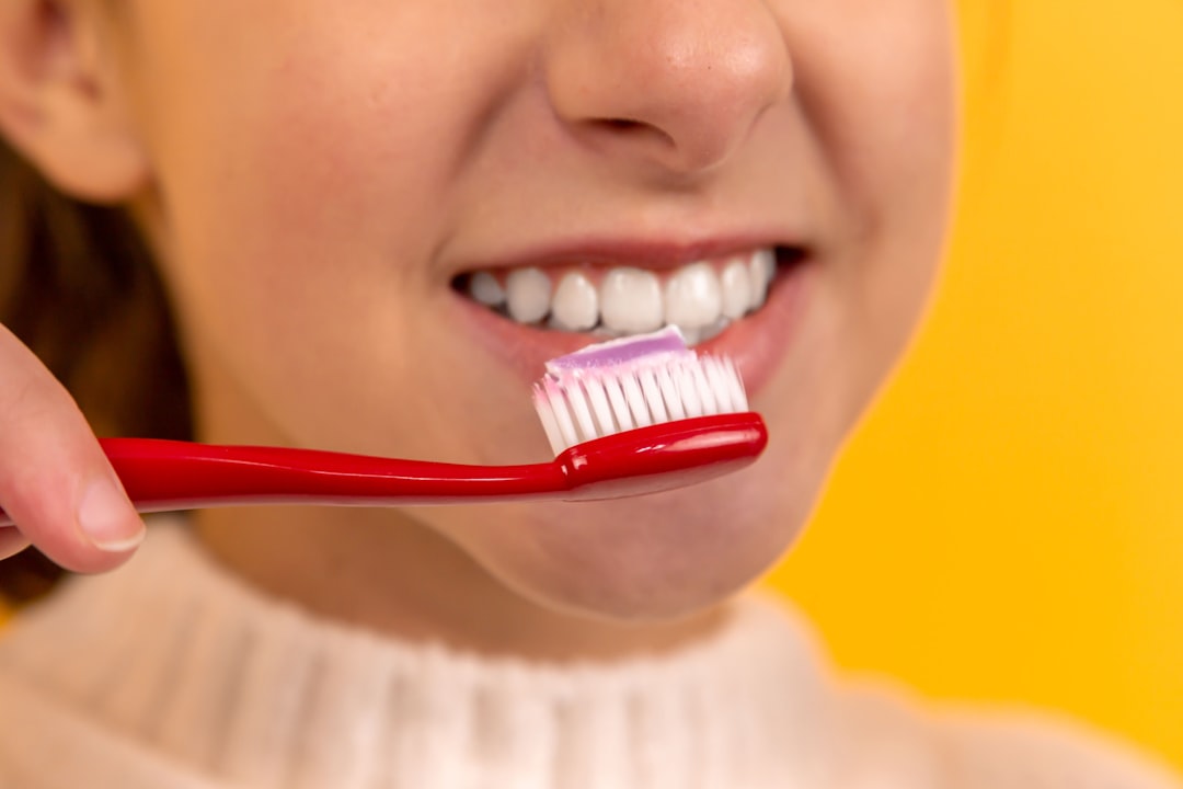 contact-img-01 Portrait of a beautiful brunette girl who smiles, laughs, brushes her teeth with a red toothbrush on a yellow background. Dentistry. Advertising. Orthodontist. Place for inscription